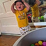 child, toddler, baby, smiling, indoors, portrait, standing, cap, yellow_shirt, pajamas, toy, ball_pit, colorful_balls, mirror, reflection, playroom, door, wood_floor, happy, photography