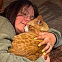 affection, cat, close_up, comfort, cozy, cuddle, face, fleece_jacket, floor, glasses, hand, hug, indoor, orange_tabby, person, pet, relaxation, ring, warm_lighting, yellow_nails