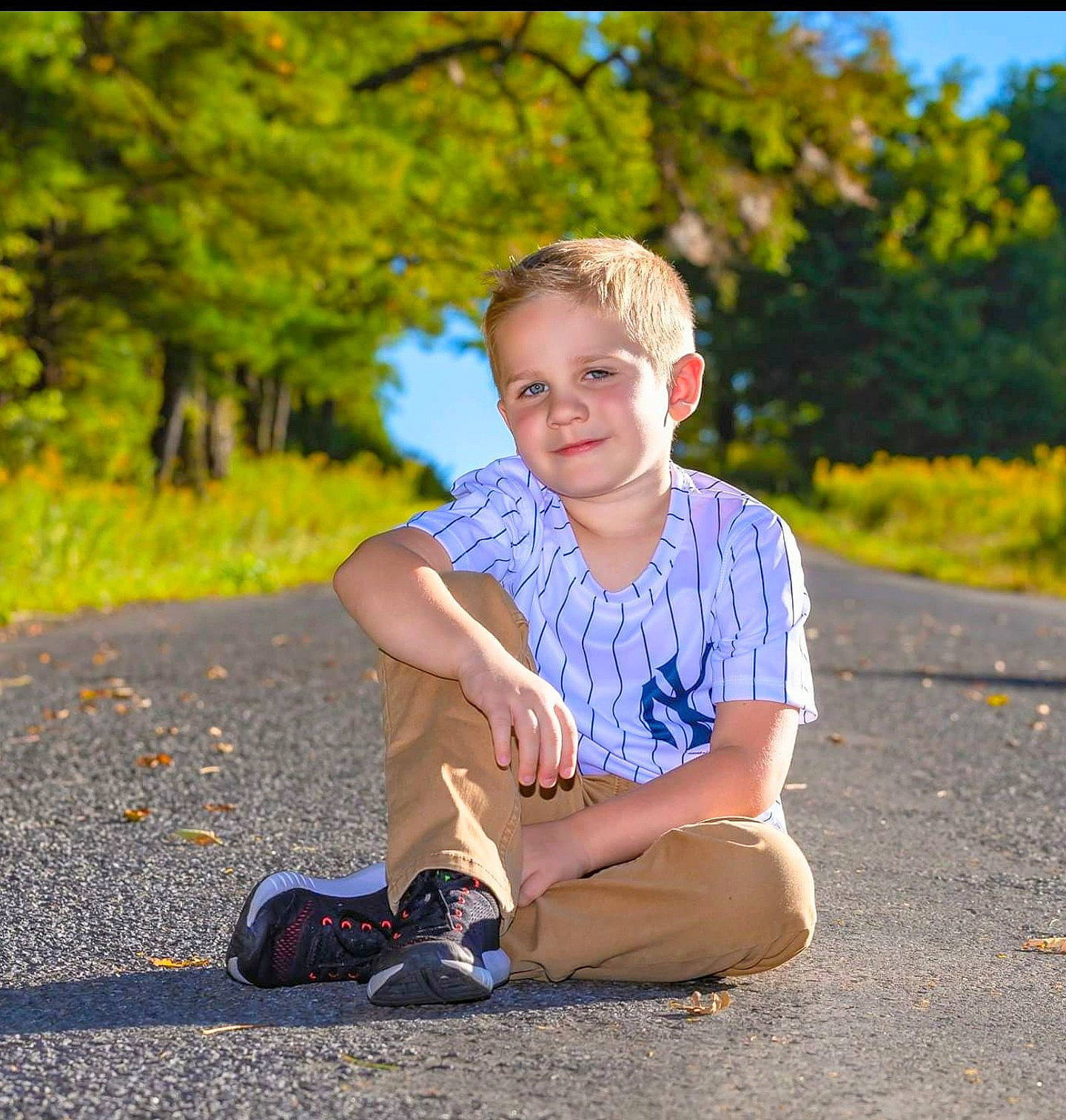 Kohen is registered to the contest to win money with this photo: asphalt, child, footwear, fun, grass, happy, joy, leaf, leisure, people_in_nature, person, photograph, photography, play, portrait_photography, sitting, smile, toddler, tree, vacation