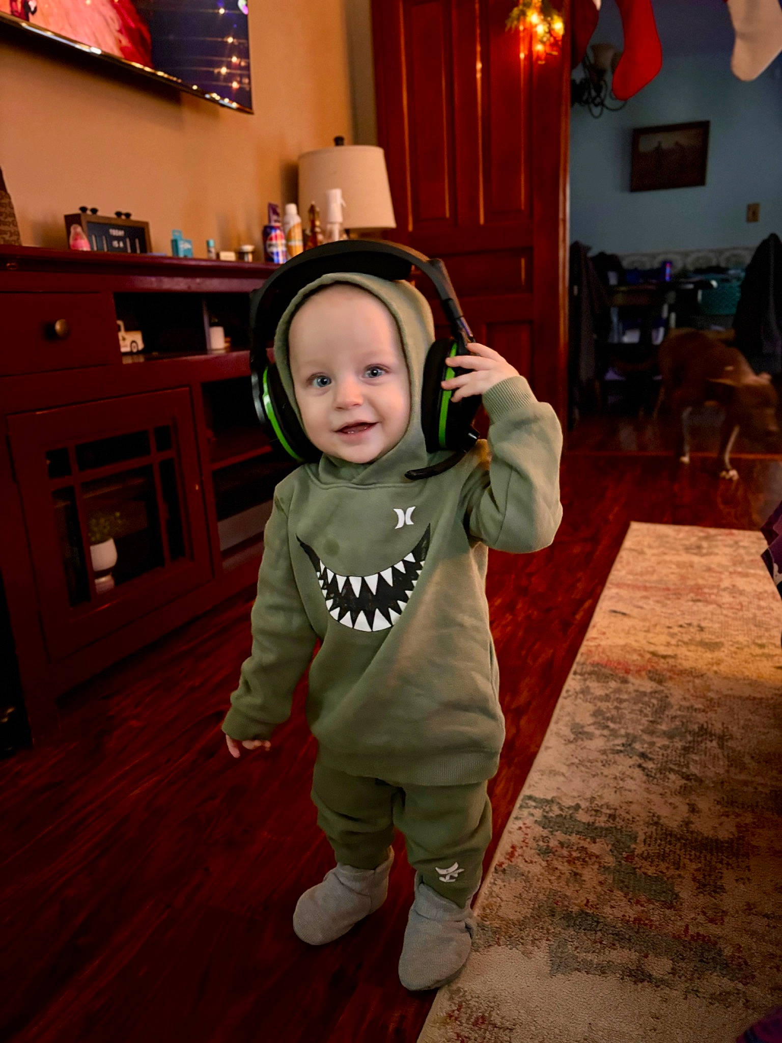 Remington is registered to the contest to win money with this photo: baby, baby_toddler_clothing, cabinetry, child, event, flooring, fun, happy, hardwood, holiday, joy, lamp, living_room, person, picture_frame, sleeve, smile, standing, television, toddler