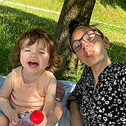 Lylou a rejoint le concours — aidez-le/la à gagner de superbes lots ! adult, blanket, bottle, casual_clothing, child, fun, glasses, grass, happy, laughing, nature, outdoor, park, person, playful, sitting, smile, summer, sunlight, tree