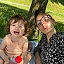 adult, blanket, bottle, casual_clothing, child, fun, glasses, grass, happy, laughing, nature, outdoor, park, person, playful, sitting, smile, summer, sunlight, tree