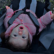 Lylou a rejoint le concours — aidez-le/la à gagner de superbes lots ! baby, blue_shoes, casual, child, clothing, curly_hair, expression, face, gravel, head, legs, outdoor, person, pink_jacket, puffy_jacket, seatbelt, stroller, surprised, toddler, young_child