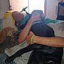 person, dog, black_dog, brown_dog, hugging, indoor, door, blanket, couch, arm, hand, collar, floor, keychain, water_bottle, sign, casual_clothing, home, light, window