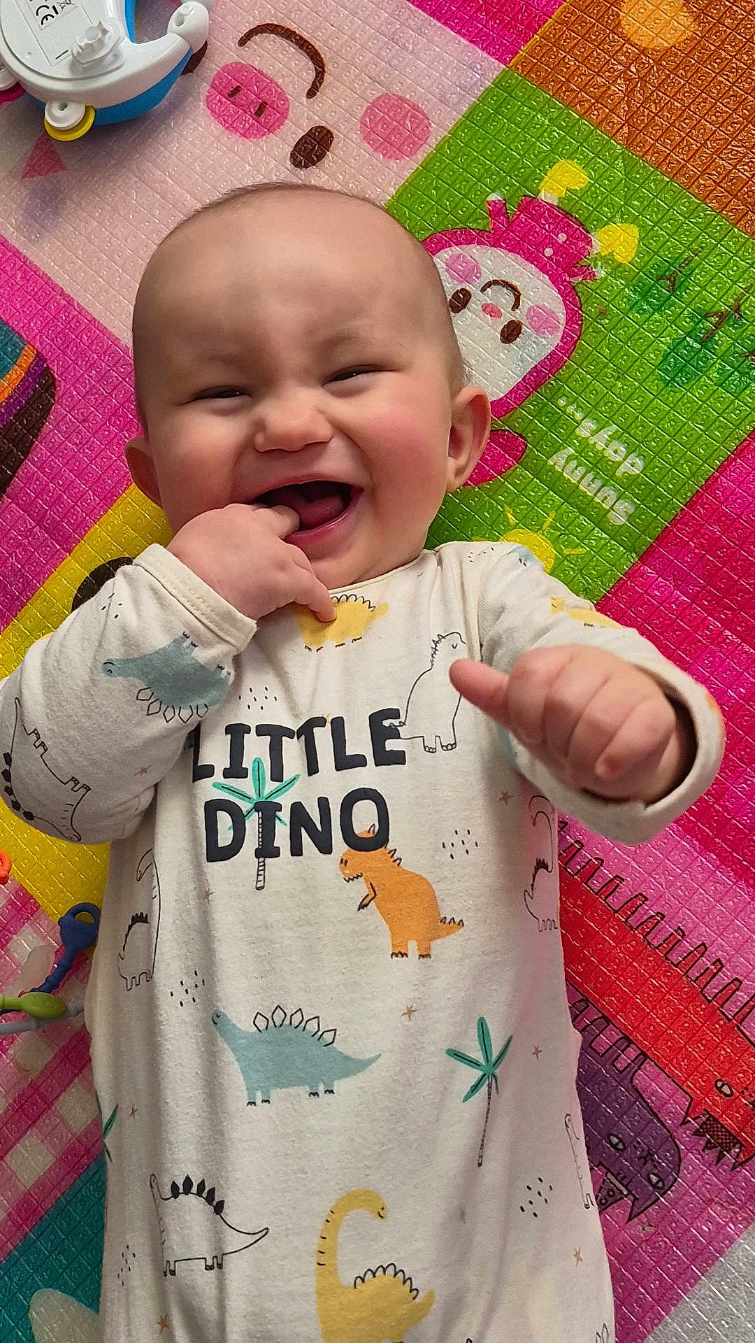 Lowen participe au concours pour gagner de l'argent avec cette photo : baby, child, smiling, dinosaur, onesie, playmat, colorful, happy, cute, infant, fingers, laughing, indoors, toy, patterned_clothing, cheerful, closeup, face, head, playtime