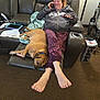 woman, dog, recliner, blanket, phone, pajamas, footrest, carpet, living_room, box, pepsi, lamp, papers, tablet, relaxing, indoors, brown_dog, casual, leather_furniture, conversation