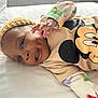 baby, bed, child, colorful_sleeves, cute, face, hand, happy, headwear, indoors, infant, knitted_hat, lying_down, mickey_mouse, person, portrait, shirt, sleepwear, smiling, white_bed