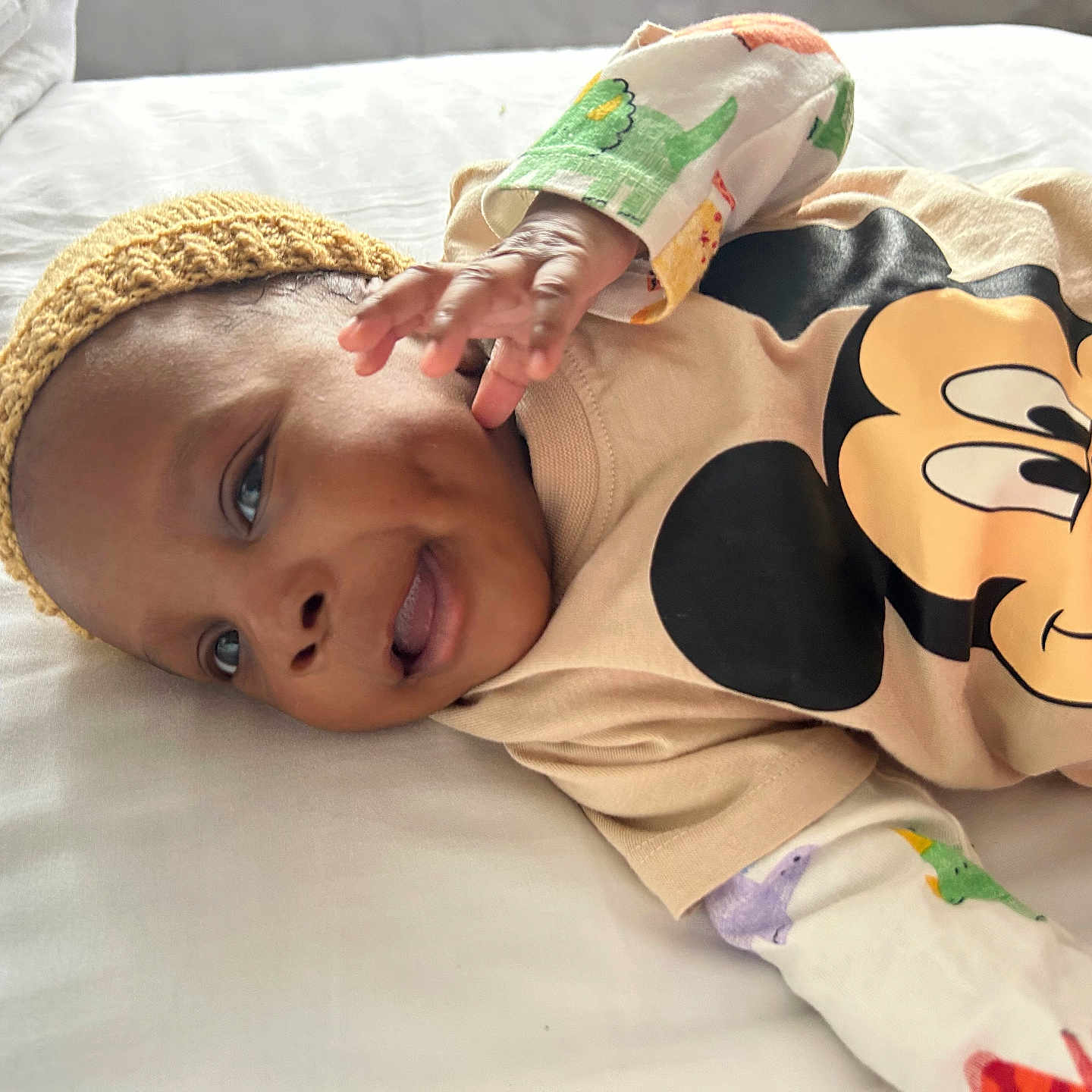 Chimsomebi is registered to the contest to win money with this photo: baby, bed, child, colorful_sleeves, cute, face, hand, happy, headwear, indoors, infant, knitted_hat, lying_down, mickey_mouse, person, portrait, shirt, sleepwear, smiling, white_bed