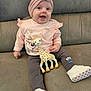 baby, child, smiling, toy, giraffe, headband, flower, pink_clothing, pants, white_shoes, couch, indoor, cute, happy, sitting, infant, playful, soft_toy, footwear, portrait