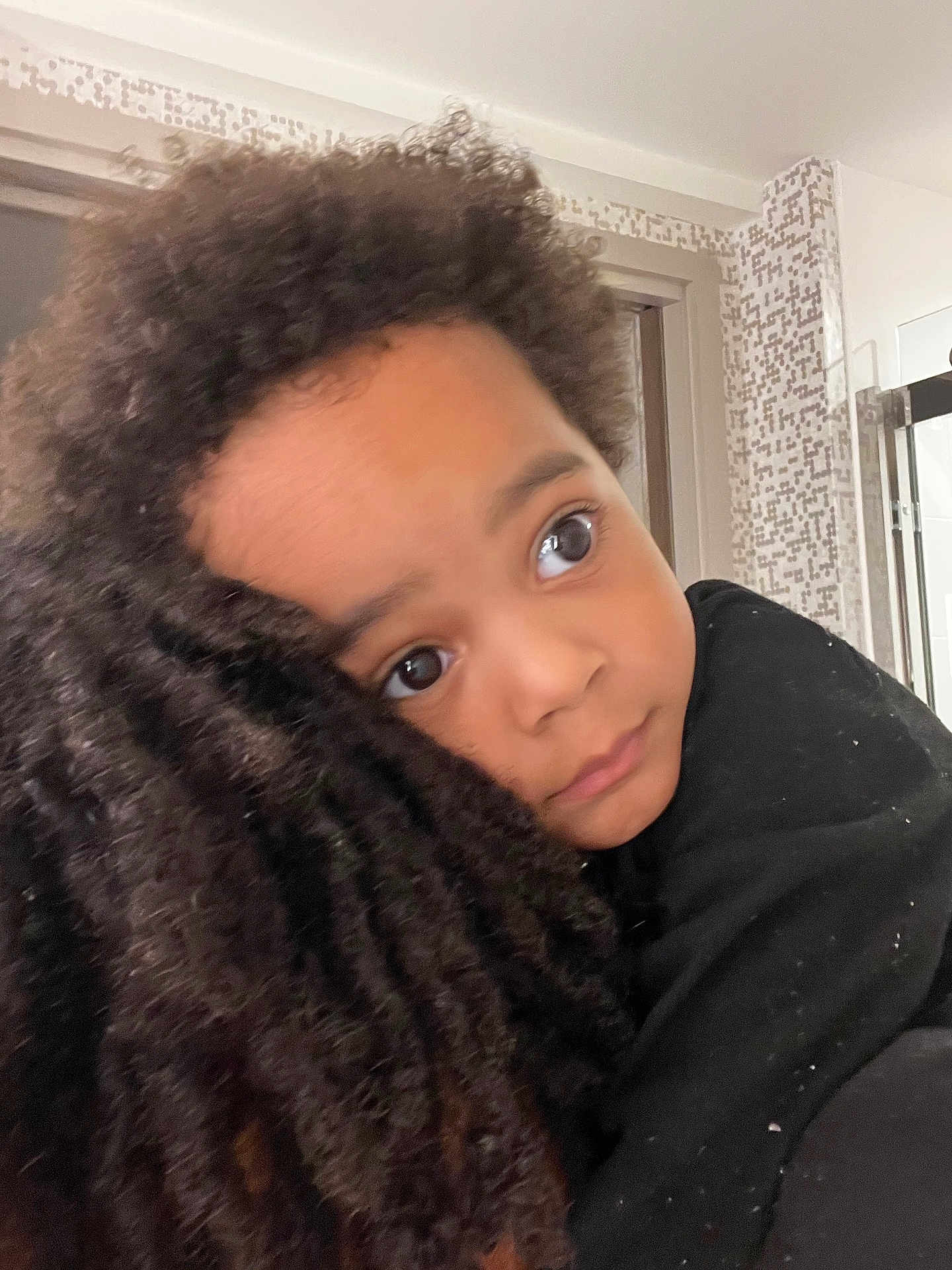 Asaiah is registered to the contest to win money with this photo: child, curly_hair, close_up, indoor, person, face, black_clothing, window, tile_wall, expression, hug, portrait, young, caring, comfort, affection, skin, human, eyes, hair
