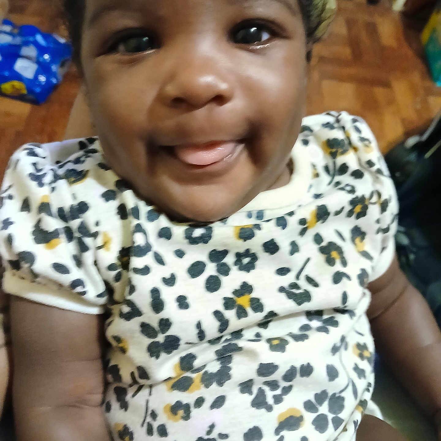 Aryanna joined the competition — help win amazing prizes! arm, baby, blurred_background, child, clothing, cute, eyes, face, floor, floral_pattern, hand, happy, indoors, infant, onesie, person, skin, smiling, tongue_out, wooden_floor