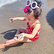 Nayla joined the competition — help win amazing prizes! child, toddler, beach, sand, sunglasses, red_swimsuit, pink_bow, sunlight, shadow, curious, summer, water, sea, play, outdoor, vacation, barefoot, portrait, young_girl, fun