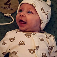 Liam is registered to the contest to win money with this photo: baby, infant, newborn, smiling, onesie, hat, bear_pattern, blanket, wooden_plaque, milestone, lying_down, cute, happy, portrait, face, child, clothing, baby_clothes, indoor, closeup
