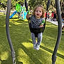 Ayden is registered to the contest to win money with this photo: child, swing, playground, outdoor, toy, grass, trees, sunlight, play_equipment, park, people, casual_clothing, smiling, happy, daytime, recreation, fun, person, active, curly_hair