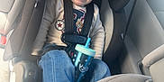 Ayden is registered to the contest to win money with this photo: toddler, child, car_seat, sippy_cup, jeans, sweater, seatbelt, car_interior, smiling, happy, seat, window, sunlight, casual_clothing, person, young_child, hair_tied_up, footwear, safety, daytime