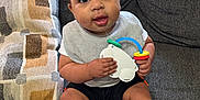 Zaylen joined the competition — help win amazing prizes! baby, child, toy, couch, pillow, drool, socks, shorts, bib, indoor, window, curly_hair, cute, seated, person, happy, playful, home, infant, portrait