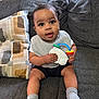 baby, child, toy, couch, pillow, drool, socks, shorts, bib, indoor, window, curly_hair, cute, seated, person, happy, playful, home, infant, portrait