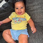 Zaylen joined the competition — help win amazing prizes! baby, child, smile, yellow_shirt, blue_shorts, couch, indoor, happy, face, person, skin, hand, foot, hair, clothing, sitting, cute, infant, relaxing, bright