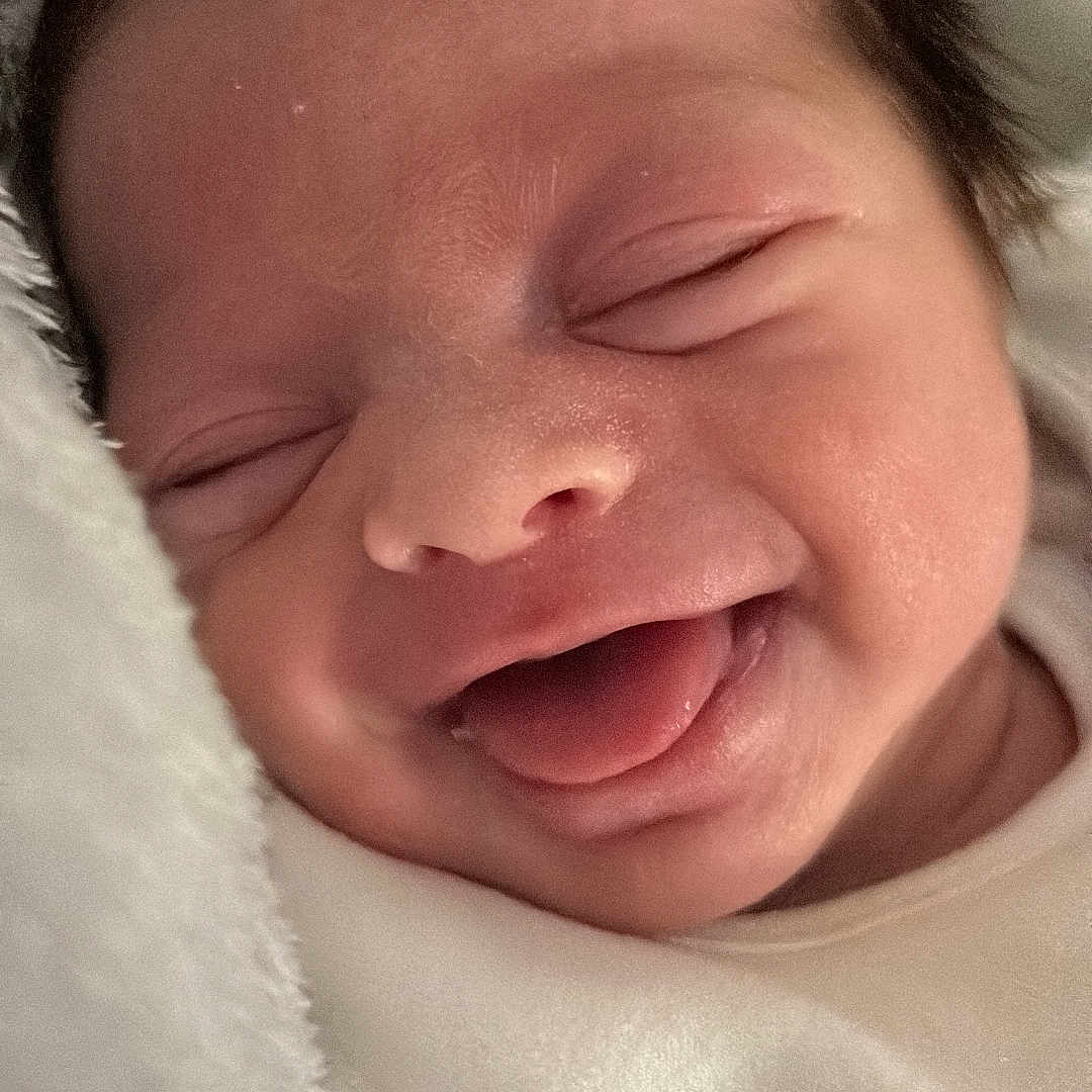 Ada is registered to the contest to win money with this photo: baby, child, close_up, cozy, cute, face, head, indoors, infant, newborn, peaceful, portrait, skin, sleeping, smiling, soft_blanket, tongue_out, warm, white_clothing, young