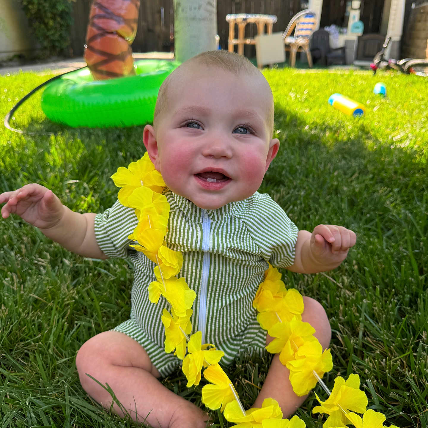 Hudson joined the competition — help win amazing prizes! baby, backyard, child, face, feet, fun, grass, greenery, happy, inflatable_toy, nature, outdoor, playground, sitting, smiling, striped_clothing, summer, sunlight, toys, yellow_flower_lei