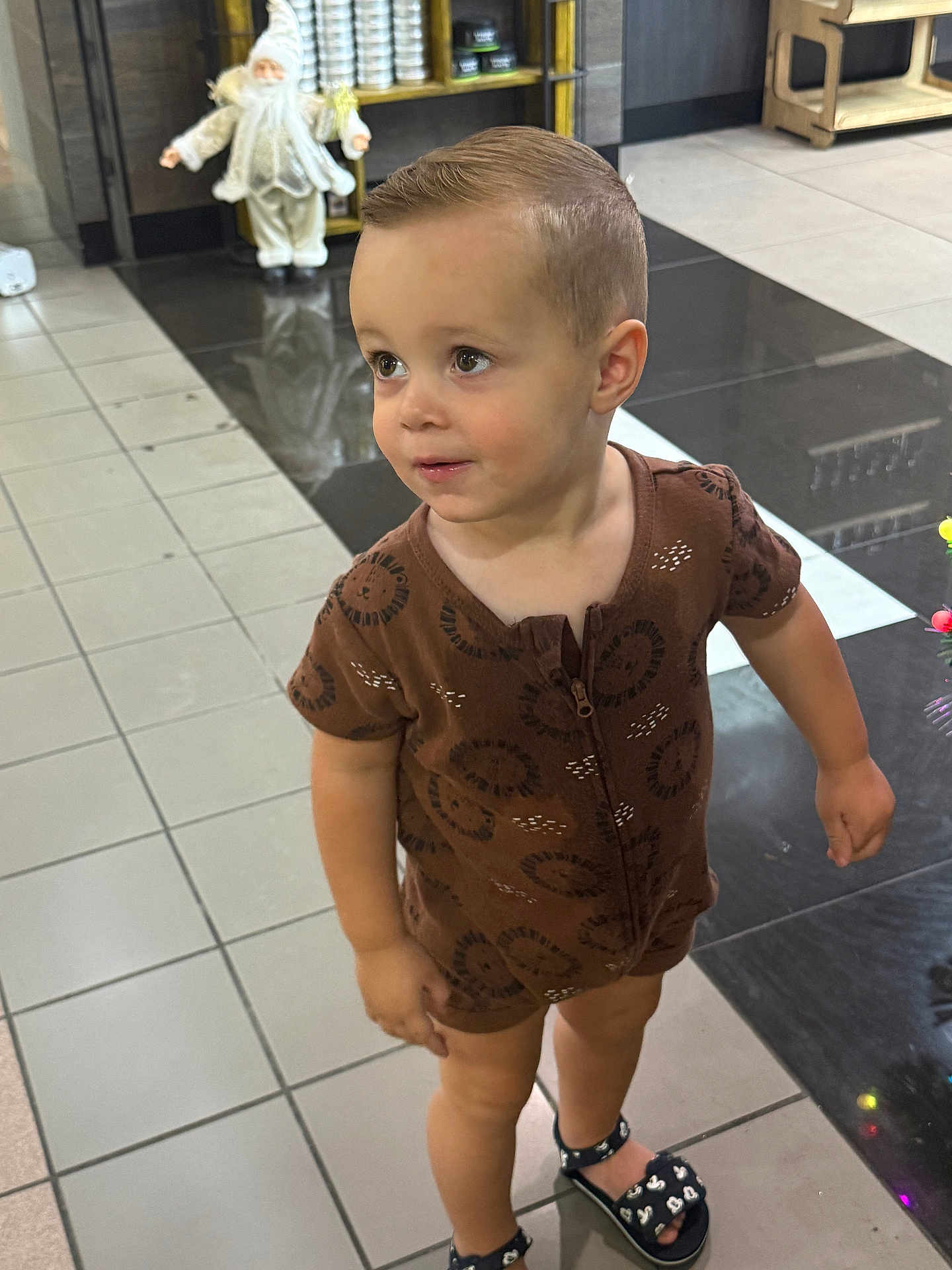 Kobi joined the competition — help win amazing prizes! brown_outfit, child, curious, cute, floor_tiles, footwear, holiday_decoration, indoor, lion_prints, looking_away, person, sandals, santa_claus_decoration, short_hair, smiling, standing, tiled_floor, toddler, toy, young_child
