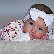 Noelle joined the competition — help win amazing prizes! baby, infant, headband, bow, blue_eyes, heart_pattern, white_clothing, lying_down, fluffy_surface, closeup, cute, child, portrait, soft_texture, young, indoors, skin, hand, face, expression