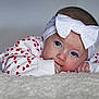 baby, infant, headband, bow, blue_eyes, heart_pattern, white_clothing, lying_down, fluffy_surface, closeup, cute, child, portrait, soft_texture, young, indoors, skin, hand, face, expression