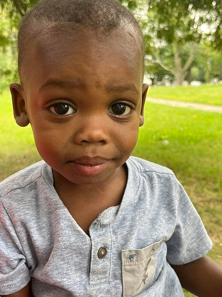 Eli is registered to the contest to win money with this photo: baby, baby_toddler_clothing, cheek, child, chin, close_up, eyebrow, fun, grass, happy, iris, lip, nose, person, plant, portrait_photography, sitting, skin, t_shirt, toddler