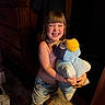 child, smiling, barefoot, stuffed_toy, plush, blue, bird, shorts, indoor, carpet, furniture, wood, happy, toy, person, cute, hair, face, hugging, night