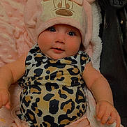 Alaska is registered to the contest to win money with this photo: baby, infant, child, hat, bow, leopard_print, onesie, blanket, plush_toy, stroller, pink, cute, portrait, close_up, smiling, eyes, chubby_cheeks, cozy, clothing, headwear