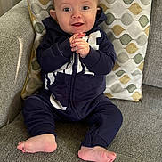 Ezra joined the competition — help win amazing prizes! baby, infant, smiling, happy, clothing, onesie, couch, pillow, patterned_pillow, indoor, child, cute, hands, feet, face, person, seated, home, cozy, texture