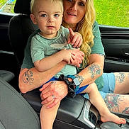 Atreus joined the competition — help win amazing prizes! child, woman, car_interior, tattoo, shorts, green_grass, window, seat, seatbelt, armrest, watch, scrunchie, barefoot, pointing, casual_clothing, daylight, portrait, family, toddler, adult