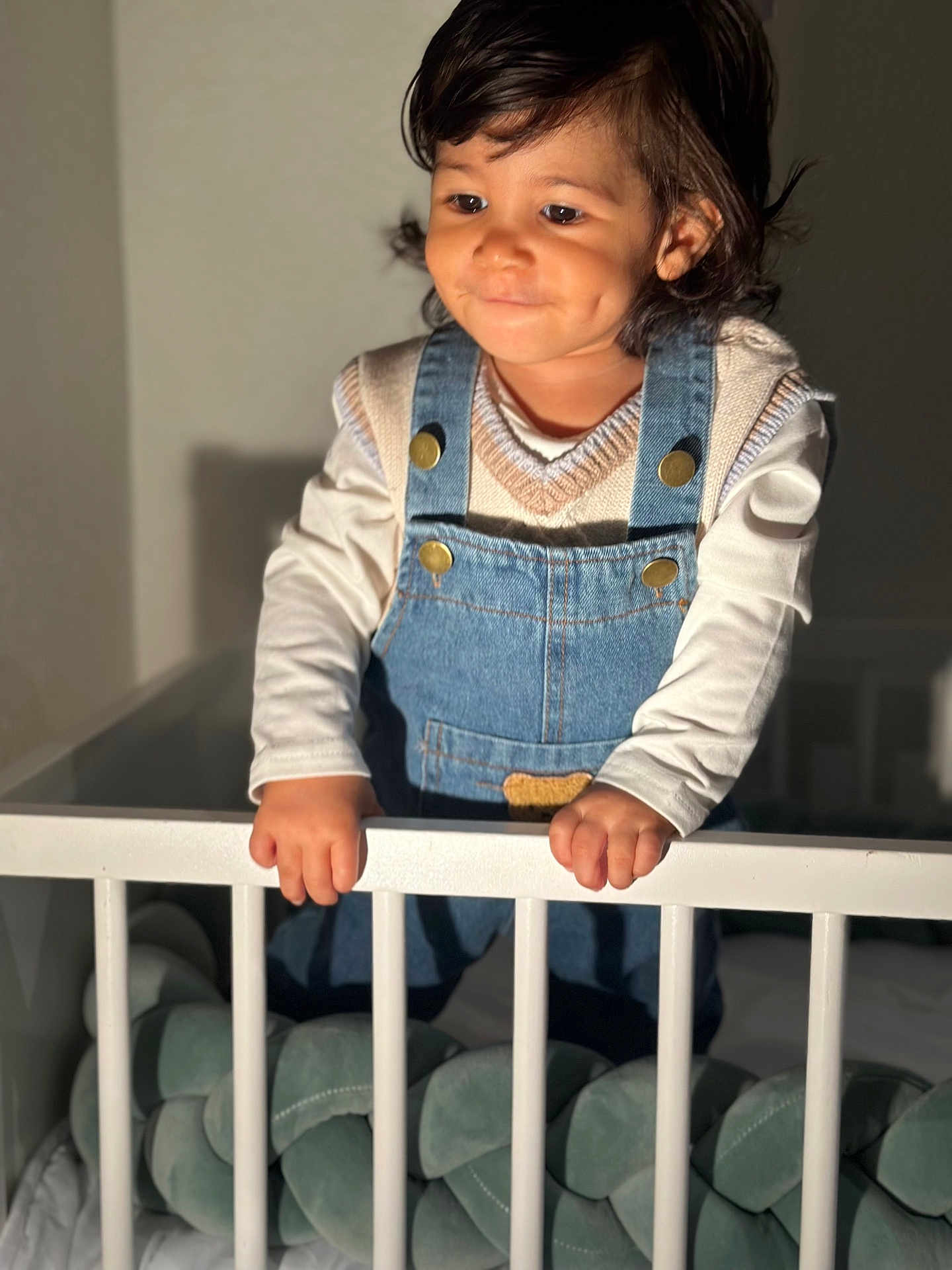Theo participe au concours pour gagner de l'argent avec cette photo : toddler, child, baby, crib, denim_overalls, sweater_vest, dimples, hands, indoor, soft_lighting, white_crib, cute, portrait, person, baby_clothes, cute_expression, standing, furniture, home, infant