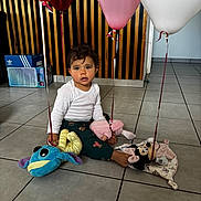 Hayana participe au concours pour gagner de l'argent avec cette photo : toddler, child, balloons, plush_toys, indoor, floor, tiles, white_shirt, pants, curly_hair, brown_eyes, toy_mouse, toy_fish, pink_balloons, white_balloon, sitting, playtime, home, cute, young_child