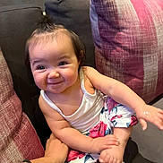 Evelyn joined the competition — help win amazing prizes! baby, child, smile, couch, pillow, hand, white_top, floral_pants, playing, indoors, cute, happy, person, sitting, young_child, cozy, hair_tie, skin, arm, foot