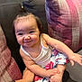 baby, child, smile, couch, pillow, hand, white_top, floral_pants, playing, indoors, cute, happy, person, sitting, young_child, cozy, hair_tie, skin, arm, foot