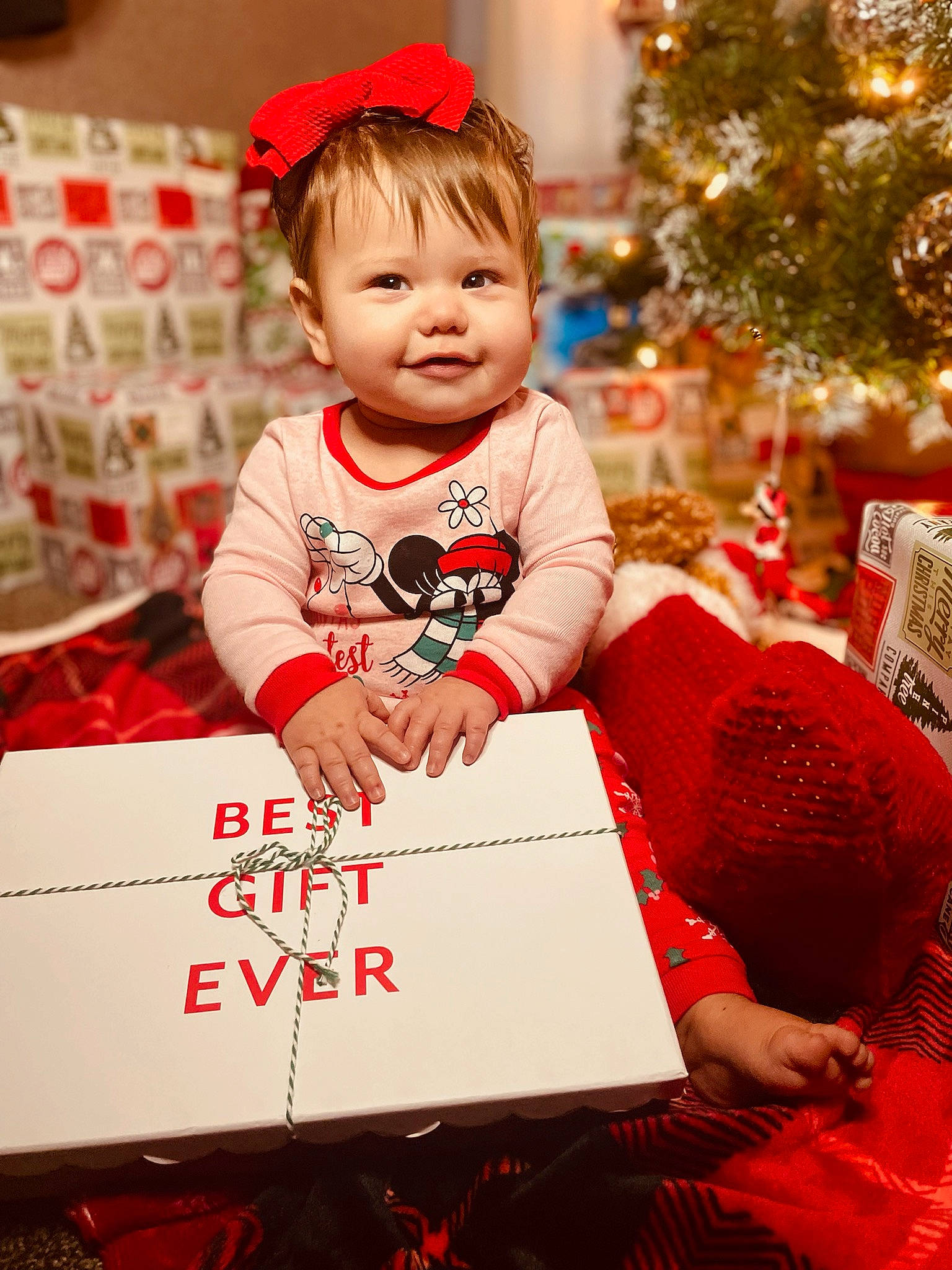 Meadow is registered to the contest to win money with this photo: baby, baby_toddler_clothing, child, christmas, christmas_decoration, christmas_ornament, christmas_tree, event, facial_expression, happy, head, holiday, joy, ornament, person, red, room, smile, snapshot, standing