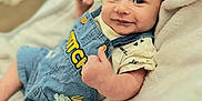 Jamison is registered to the contest to win money with this photo: arm, baby, blanket, child, clothing, cute, denim_overalls, expression, face, happy, head, indoors, infant, person, portrait, relaxed, skin, smile, soft_texture, thumbs_up