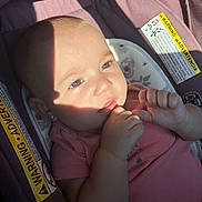 Jenny joined the competition — help win amazing prizes! baby, infant, car_seat, child, face, hand, shadow, sunlight, pink_shirt, warning_label, seat, cute, skin, portrait, closeup, young_child, sitting, indoors, expression, small_hands