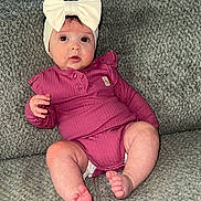 Hazel joined the competition — help win amazing prizes! baby, infant, child, headband, bow, purple_outfit, couch, gray_couch, texture, foot, toes, sitting, curious, wide_eyes, indoor, cozy, comfortable, clothing, person, portrait