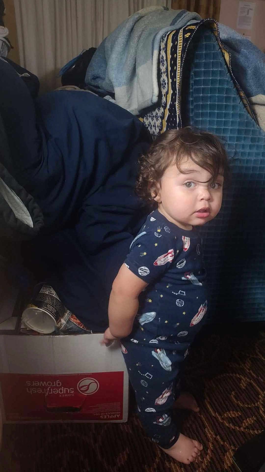 Swiss joined the competition — help win amazing prizes! toddler, child, indoor, pajamas, space_theme, curly_hair, box, blanket, can, carpet, person, standing, looking, furniture, home, casual, expression, barefoot, young_child, curious