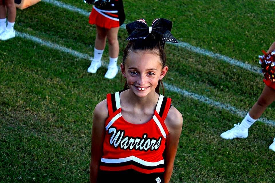 Bella is registered to the contest to win money with this photo: black, cheerleading_uniform, event, grass, happy, human_leg, jersey, joy, person, player, red, smile, sports, sports_uniform, sportswear, team, team_sport, thigh, tournament, uniform