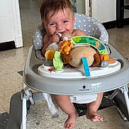 Jules participe au concours pour gagner de l'argent avec cette photo : baby, walker, toy, plush_toy, floor, tile_floor, indoor, child, smiling, chewing, clothing, foot, seat, furniture, polka_dot, happy, person, home, doorway, playtime