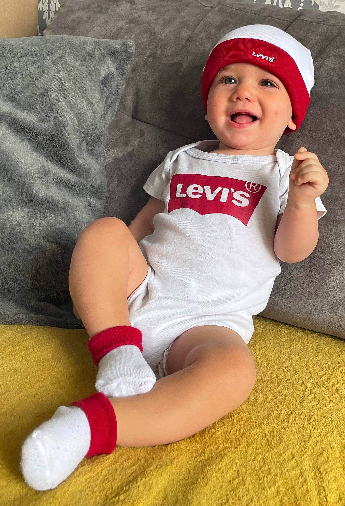 Warren participe au concours pour gagner de l'argent avec cette photo : baby, baby_toddler_clothing, baseball_cap, cap, comfort, couch, elbow, face, finger, happy, hat, headwear, human_leg, knee, lap, leg, person, sleeve, smile, sock