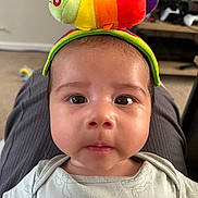 Kai is registered to the contest to win money with this photo: baby, infant, face, eyes, toy, plush_toy, caterpillar, headwear, onesie, indoor, carpet, furniture, shelf, gaming_controller, curious, closeup, child, person, cute, soft_toy