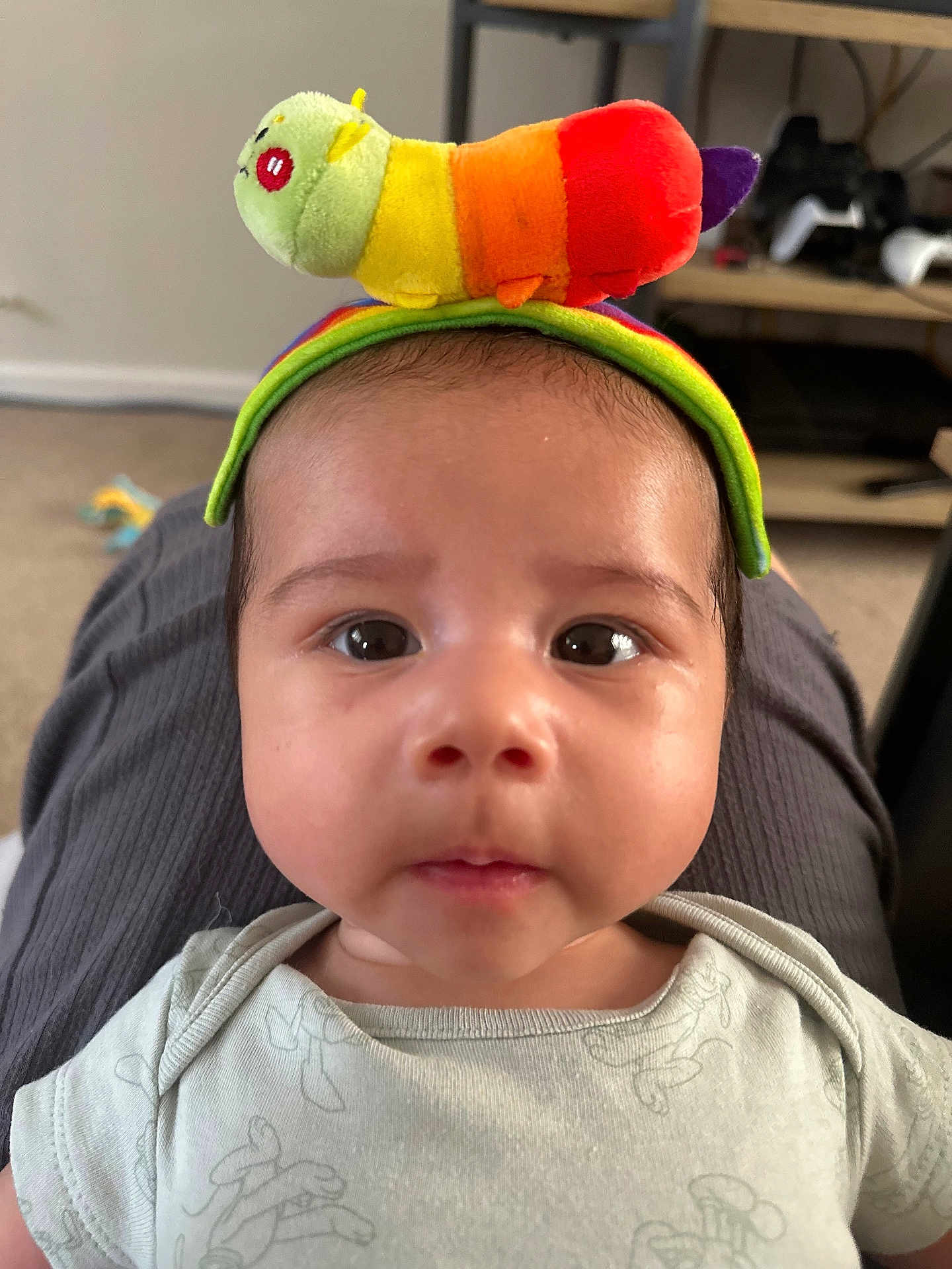 Kai is registered to the contest to win money with this photo: baby, infant, face, eyes, toy, plush_toy, caterpillar, headwear, onesie, indoor, carpet, furniture, shelf, gaming_controller, curious, closeup, child, person, cute, soft_toy