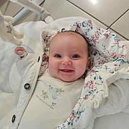 Ava a rejoint le concours — aidez-le/la à gagner de superbes lots ! baby, smiling, blanket, floral_pattern, white_clothing, infant, face, happy, lying_down, indoor, tile_floor, cute, child, person, portrait, cozy, button, sleeve, head, newborn