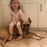 Rudy is registered to the contest to win money with this photo: barefoot, brown_dog, cabinet, carpet, child, companionship, curly_hair, cute, dog, floor, floor_rug, glasses, home, indoor, pajamas, pet, playful, relaxed, tongue_out, young_child