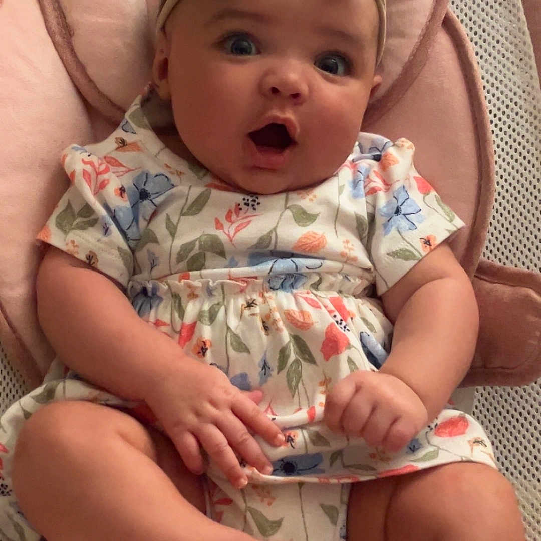 Eliana is registered to the contest to win money with this photo: baby, bow, child, clothing, comfort, cute, expression, feet, floral_dress, hands, headband, indoors, infant, person, pink, plush_seat, portrait, sitting, skin, surprised