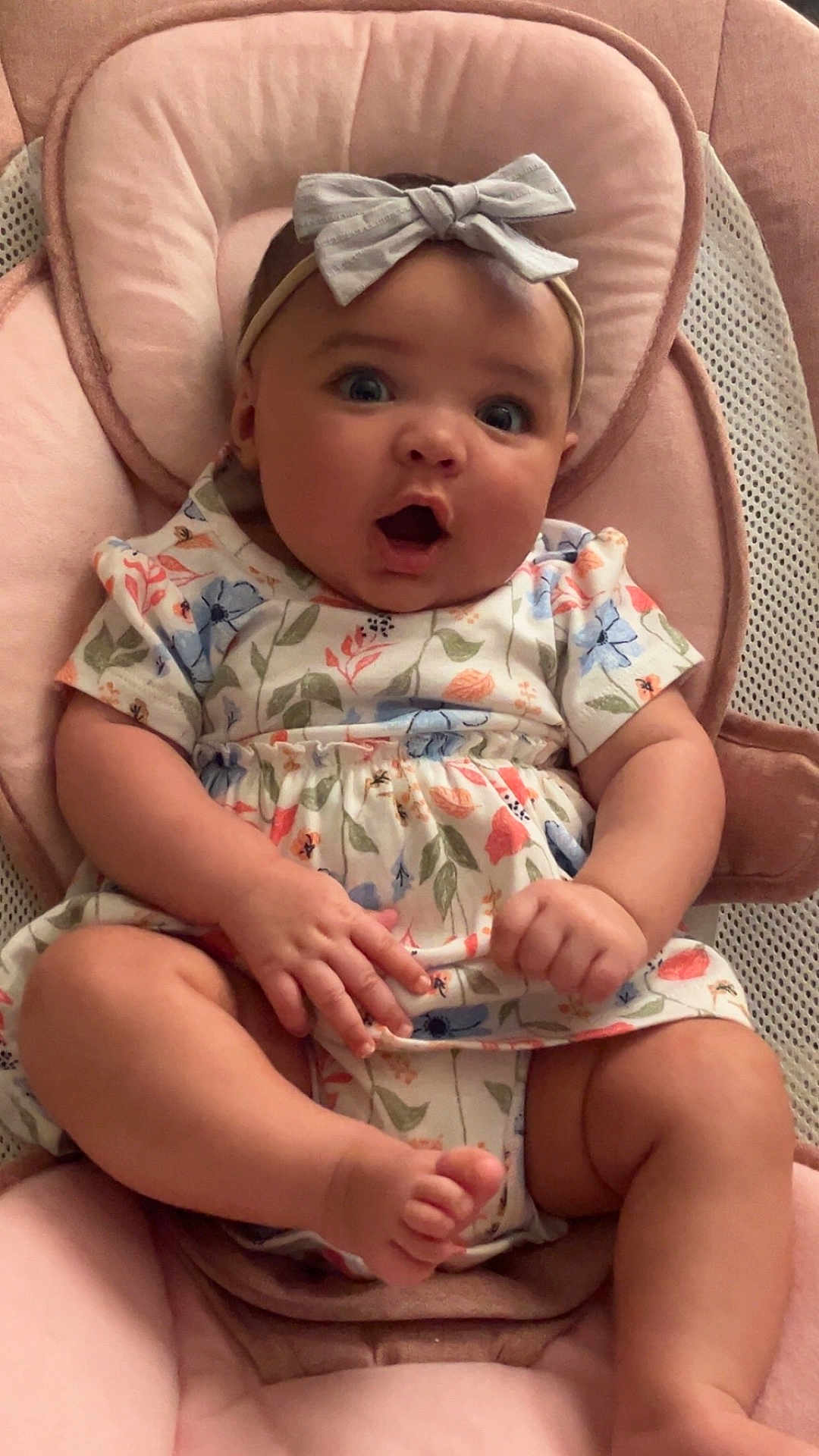 Eliana is registered to the contest to win money with this photo: baby, infant, child, surprised, pink, headband, bow, floral_dress, sitting, plush_seat, cute, indoors, skin, hands, feet, expression, person, portrait, clothing, comfort